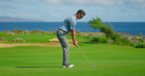 Man playing golf on beautiful course by the ocean, swinging and hitting golf ball, slow motion