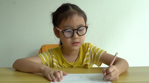 Cute smart primary school child girl learning writing doing math homework sit at home table, adorable pretty little preschool kid studying alone making notes, children elementary education concept