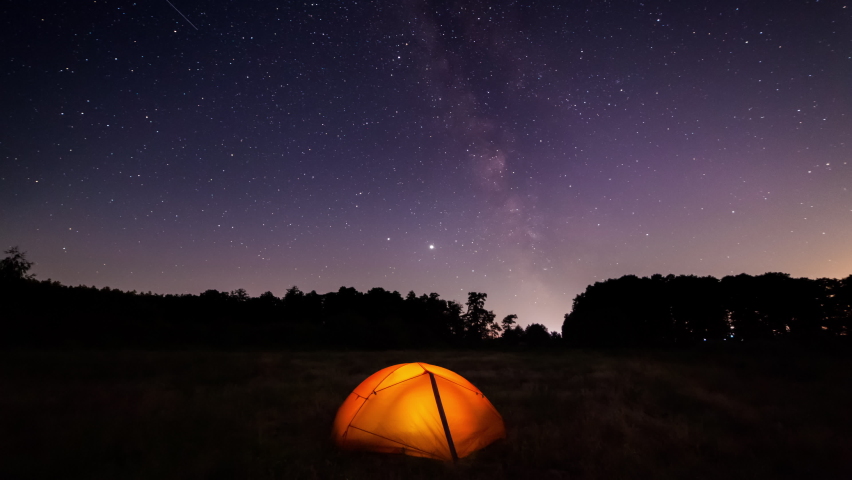 Orange iluminated tent in the forest under the starry sky. Timelapse of the starry sky with the Milky Way | Shutterstock HD Video #1060640068