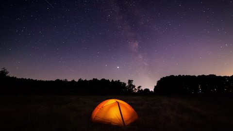 Orange iluminated tent in the forest under the starry sky. Timelapse of the starry sky with the Milky Way