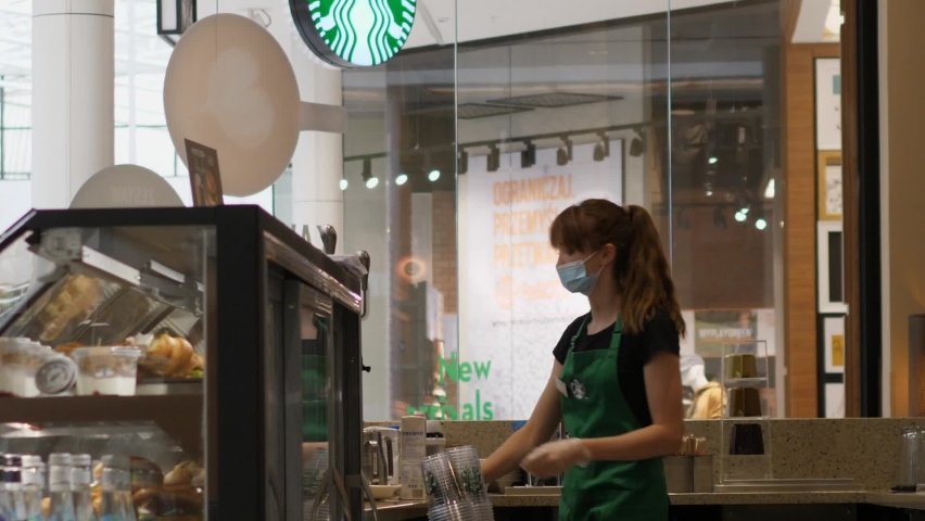 Female barista wearing face mask cleans her workspace. Starbucks coffeehouse during covid-19 pandemic.Warsaw-Poland-2020