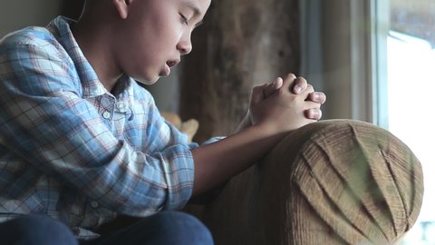 Boy praying on sofa at home, church in home, Home church during quarantine coronavirus Covid-19, Religion concept.