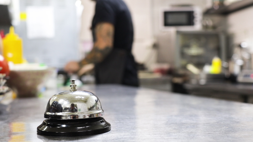 Silver Call Bell on table, chefs in a restaurant on background. cooking in the kitchen Royalty-Free Stock Footage #1060642309