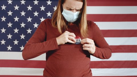 Voting woman putting on Vote button with face mask at elections and american flag.