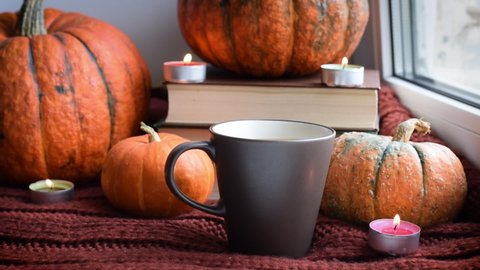 Cozy Hygge scene with sweater and candles. Orange pumpkins and cup of tea ore coffee.  Halloween concept, cozy home, aromatherapy.