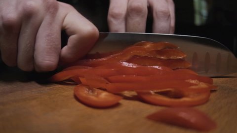 chef quickly cuts red pepper on a wooden board with a knife