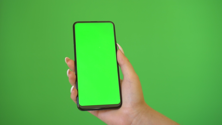 Woman hand holds a smartphone with greeen screen over a green background. | Shutterstock HD Video #1060650565