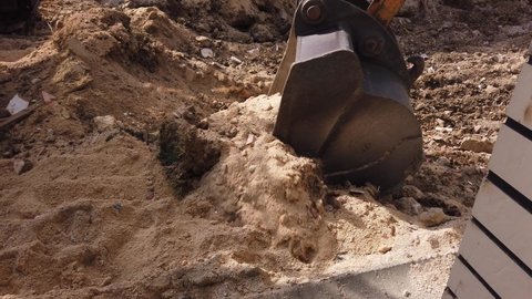 Dust flies in air. Road repair work. excavator metal bucket digs ground before laying asphalt.