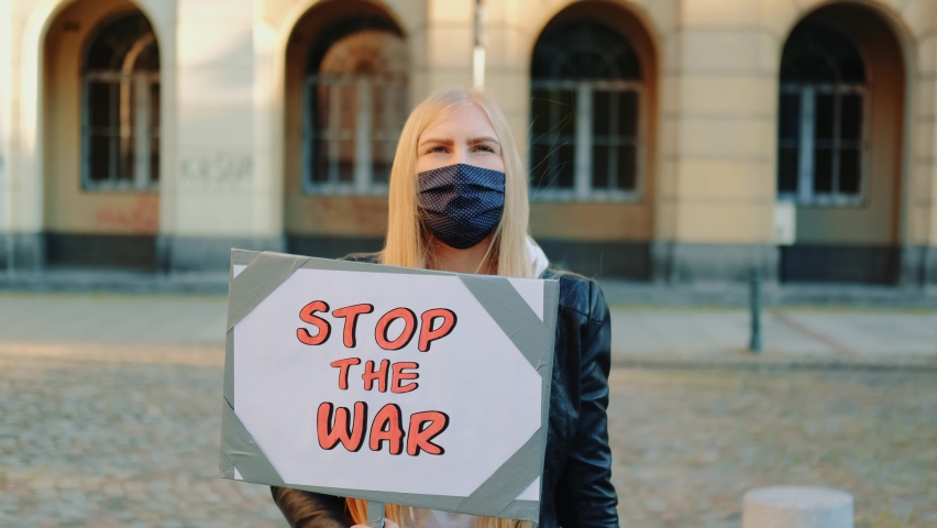 Young woman wearing medical mask calling to stop the war by holding steamer. Protest walk in the city center.