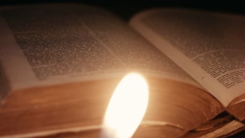 dolly shot of a man turning pages through an ancient book lit by candles