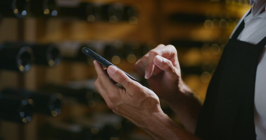 Modern farmer or winemaker is using winery online commerce applications on a smartphone for checking customer service and selling orders summary of his wine production in a wine cellar. Royalty-Free Stock Footage #1060657846
