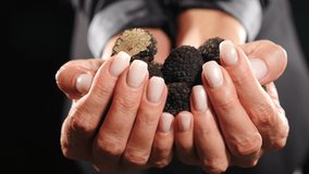Elegant female hands holding and offering tubers of black truffles. Rare black truffle mushroom on dark background. Close-up shot. Luxury expensive food, gourmet in restaurant. 4 k video