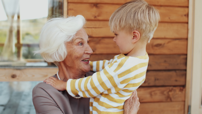 Cheerful senior grandmother speaking with cute little boy and hugging him with love while sitting on outdoor terrace on summer day Royalty-Free Stock Footage #1060662295