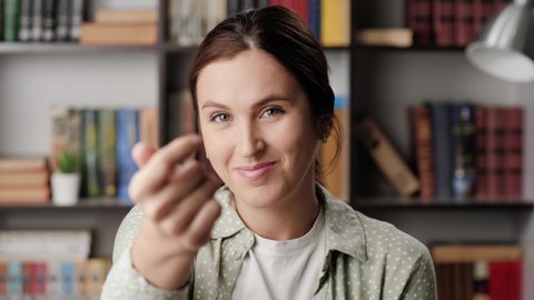 Woman beckoning finger gesture. Happy positive smiling woman in office or apartment looks at camera and points with finger and invite gesture asks to come to her