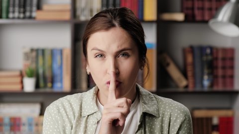 Shh, woman secret finger. Suspicious woman in office or apartment looks at camera and brings her index finger to her mouth lips and she say shhh