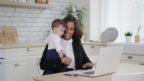 Mixed race business woman working at home online on a laptop while holding her young child. Remote work in a comfortable environment