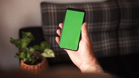 Handheld Camera: Point of View of Man at Modern Room Sitting on a Chair Using Phone With Green Mock-up Screen Chroma Key Surfing Internet Watching Content Videos