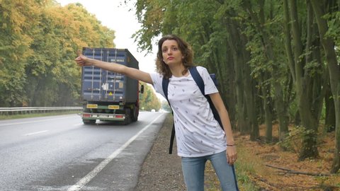 Young woman with dark blue backpack catches car on road, auto stop, traveling alone, summer vacation adventure concepts.