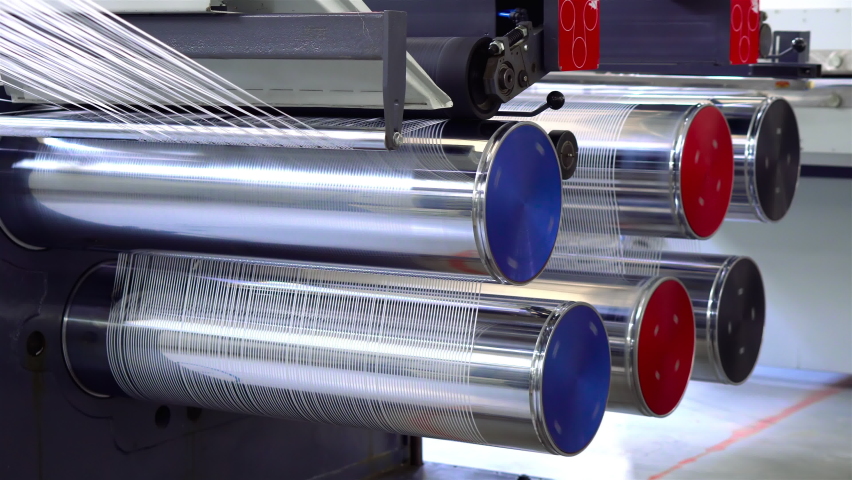 Production of white polypropylene flat yarn for the production of industrial bags. The shafts are spinning. Cellophane moves between the shafts. Polypropylene Cloth is cut into thin flat threads. | Shutterstock HD Video #1060680331