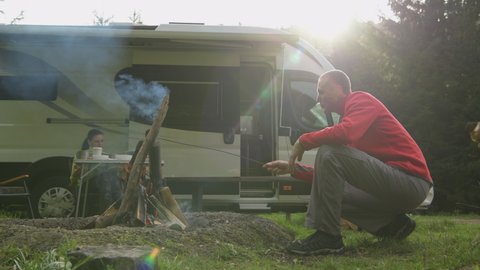 RV Park Campfire and Couple Hanging Together in Front of Their Modern Camper Van RV