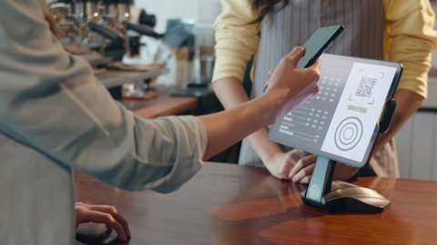 Young Asia female self service use mobile phone pay contactless with tablet at cafe restaurant. Girl barista talking receive orders from customer at bar counter in coffee shop. Owner small business.