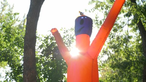 Orange Wacky Waving Inflatable Tube. Waving Flailing Arms Wacky Tube Man on a Background of Green's Trees in the Park. Funny Inflatable Figure Dancing in the Wind. Air Power Dancer Guy. Adventure park