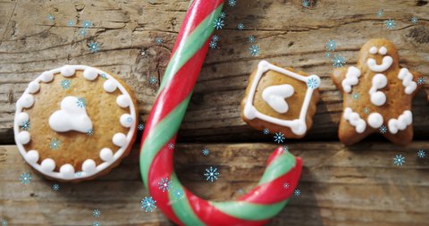 Animation of Christmas gingerbread man cookies and candy cane with falling snowflakes on wooden surface. Christmas celebrations concept digitally generated image.