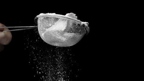 Flour sifting with sieve for pie and cupcake making. Chef confectioner sifts powdered sugar or flour in sieve slow motion isolated on black background. cooking desserts with sugar powder.