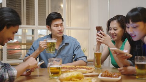 Young attractive asian man drink beer feeling unhappy lonely during friends addicted social media on mobile phone ignoring gathering party dinner. Boredom of youth culture.