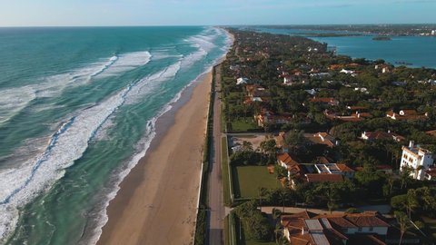 Aerial view above traffic on a the s ocean blvd road, while waves hit the Municipal Beach, during sunrise, in Palm Beach, Miami, Florida, USA - tilt up, drone shot