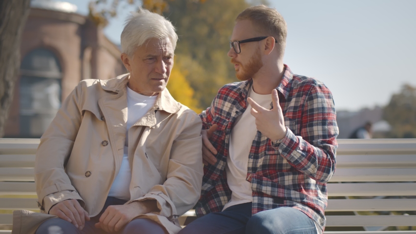 Senior father with adult son talking relaxing on bench in city center