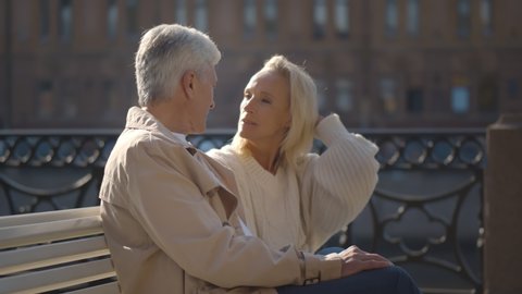 Happy senior loving couple embracing and relaxing sitting on bench in city
