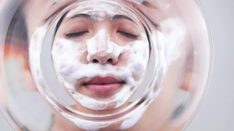 The woman is immersing the bubbles on her face in the water.