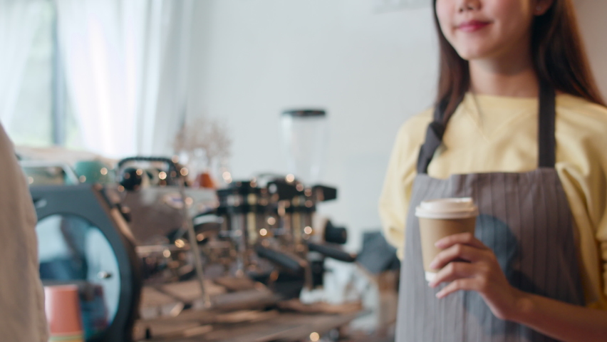 Young Asia female barista serving take away hot coffee paper cup to consumer standing behind bar counter at cafe restaurant. Owner small business, food and drink, service mind concept. | Shutterstock HD Video #1060698748
