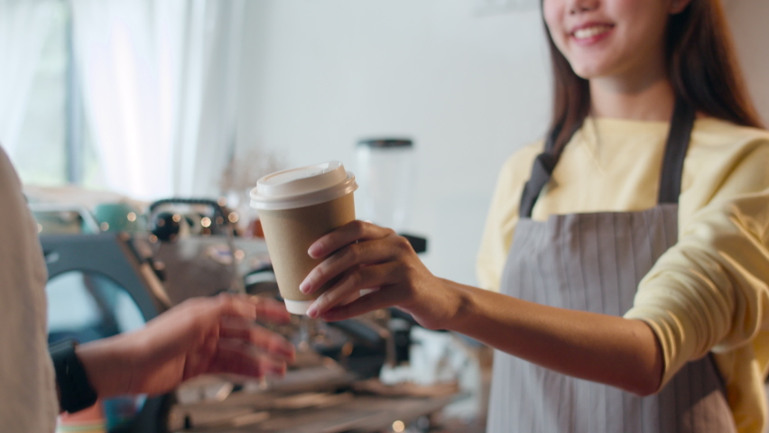 Young Asia female barista serving take away hot coffee paper cup to consumer standing behind bar counter at cafe restaurant. Owner small business, food and drink, service mind concept. | Shutterstock HD Video #1060698748