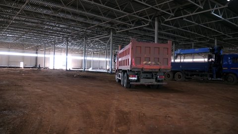 KAZAN, TATARSTAN/RUSSIA - SEPTEMBER 03 2019: Color tipper truck with dirty workbody drives along spacious workshop inner premise with dirt floor of future production complex on September 03 in Kazan