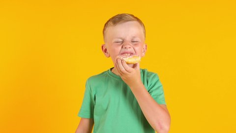 Funny little boy eating tasty donut on color background