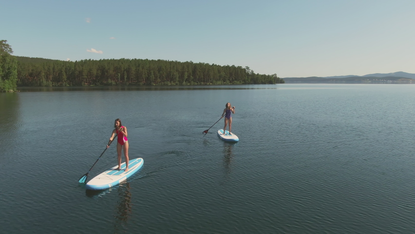 Sequence of footages showing female best friends in sports swimwear doing stand up paddle surfing in lake
