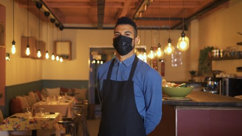 African American businessman wearing a protective black face mask and standing at his restaurant during Coronavirus. Proud owner with his arms crossed and looking at the camera with a defiant gaze.
