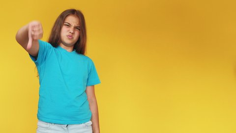 Dislike gesture. Disgusted kid. Wrong choice. Bad idea. Skeptic disappointed young girl in blue t-shirt denying offer with thumbs down isolated on yellow copy space background.