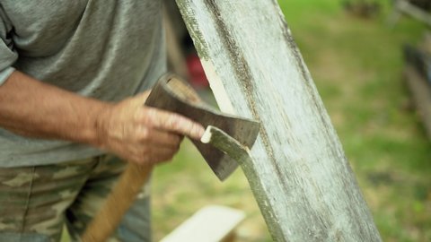 The carpenter cuts off the edge of the board with a sharp ax. Woodwork.