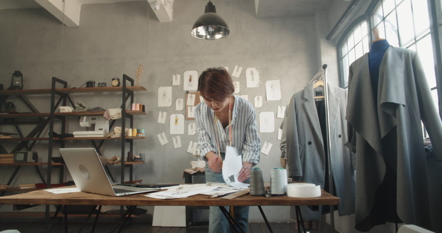 Hipster asian clothes designer working with her sketches, drawing them on graphics tablet, designing her new collection - small business, fashion concept 4k footage | Shutterstock HD Video #1060702648