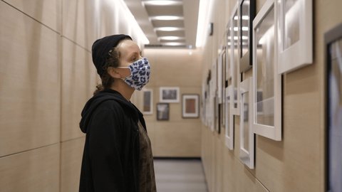 Young woman wearing face mask looking at pictures in photography gallery. Educational activities during covid-19 pandemic