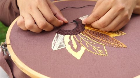 Woman stitching embroidery flower and leaves on dark cloth