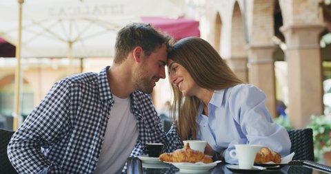 An young carefree romantic happy couple in love is having fun and drinking coffee while enjoying a breakfast together in city center cafeteria on a weekend in a sunny day.