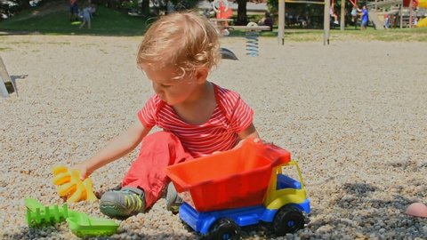Happy little child having fun playing with his colorful truck in the park, beautiful summer sunny day in children playground