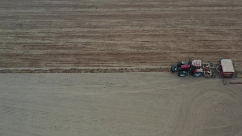 Tractor with sowing machine sowing on dried spring field, aerial view 