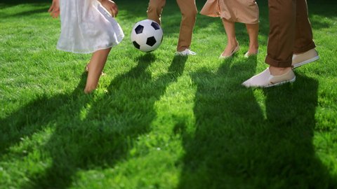 Closeup of parents and kids feet playing with soccer ball in green park. Active family playing football. Children legs trying to catch ball during game. Happy family enjoying summer outdoor activity