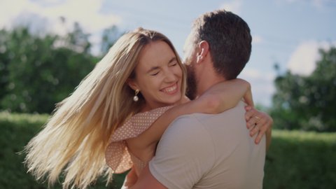 Portrait of happy woman hugging man in park. Closeup cheerful husband turning around woman on hands. Smiling man and woman laughing outdoors. Romantic couple enjoying leisure time together