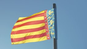Regional flag of the Valencian Community blowing in the wind against a clear blue sky.